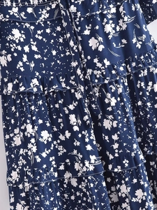 Détail de robe à fleurs bleu marine avec volants étagés et ceinture à nouer fine
