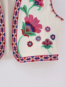 Detailed close-up of vibrant floral embroidery and geometric borders on the beige vest