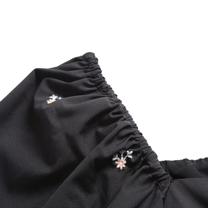 Close-up of pink flower embroidery and elastic shirring detail on black fabric