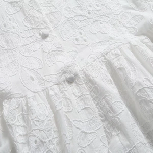 Gros plan sur les broderies florales complexes et boutons en tissu d'une robe blanche