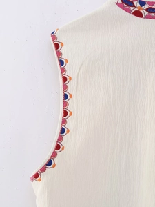 Macro shot of ethnic floral embroidery and pleated fabric on white sleeveless vest