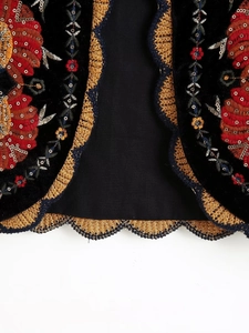Détail macro d'une broderie florale rouge sur gilet en velours noir avec bordure crochetée dorée