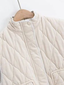 Detail of cream wave-quilted vest jacket with snap buttons on a wooden hanger