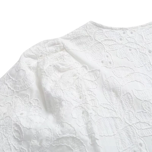 Gros plan d'une robe blanche avec broderie florale détaillée et dentelle ajourée à l'épaule