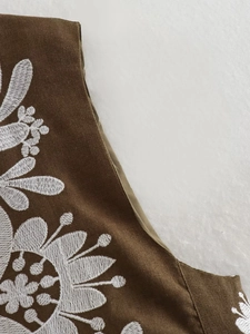 Close-up of white floral embroidery on dark brown vintage fabric with piped edges