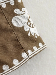 Close-up of white floral paisley embroidery on brown cotton linen vintage vest fabric