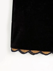 Détail de l'ourlet en velours noir avec dentelle tricotée dorée et bleue à bord ondulé