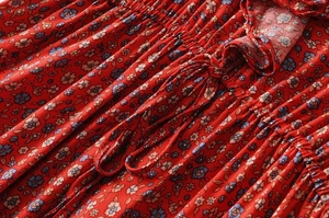 Detail of red floral dress featuring elastic shirring, drawstrings, and ruffle hem accents