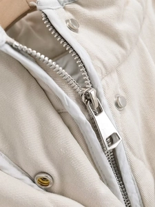 Detailed close-up of beige quilted vest featuring silver metal zipper and snap buttons