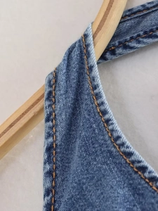 Detailed close-up of blue washed denim fabric with classic orange contrast stitching