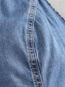 Macro shot of light blue washed denim fabric with yellow double stitching details