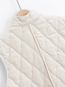 Detailed view of cream quilted puffer vest with stand collar and wavy stitching patterns