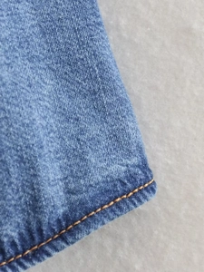Detailed close-up of dark blue denim fabric with orange contrast stitching and hem finish