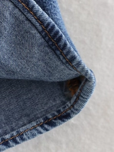 Detailed close-up of blue denim fabric with orange contrast stitching and edge binding