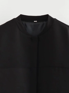 Detail of a black bomber jacket stand collar with white neck label on smooth woven fabric