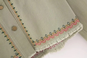 Macro shot of olive denim jacket featuring vibrant geometric embroidery and raw fringe edges