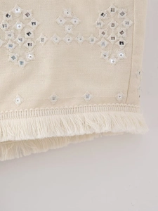 Macro detail of Y2K beige top featuring bohemian embroidery, silver sequins and fringe trim