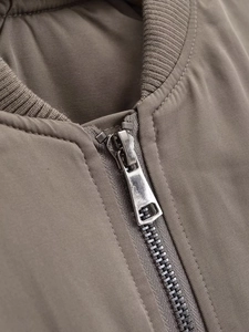 Detalle de cremallera metálica y cuello alto acanalado en la chaqueta bomber kaki