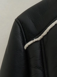 Close-up of black leather jacket featuring contrast white faux shearling trim and grain texture