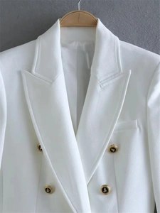 Detail of white double-breasted blazer showing gold embossed buttons and sharp peaked lapels