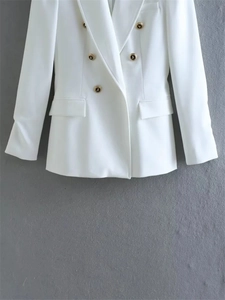 Detail view of white double-breasted blazer featuring embossed gold decorative buttons