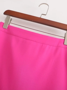 Détail de la taille d'une jupe rose taille haute sur un cintre en bois avec clips en métal
