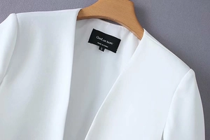 Close-up detail of the black brand label and size tag on a white V-neck cape blazer