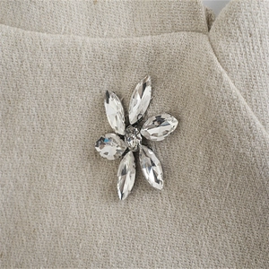 Vista macro di una spilla a fiore argento con petali di cristallo su tessuto beige