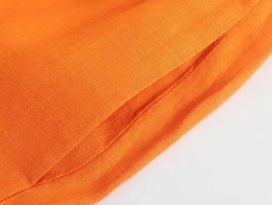 Détail de la texture du tissu en lin orange et des coutures de la poche latérale du pantalon