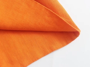 Gros plan du tissu en lin orange montrant la texture détaillée et la couture d'ourlet
