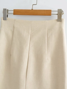 Detailed close-up of high-waisted beige linen skirt with pleated texture and fine fabric