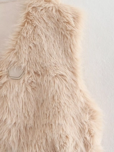 Détail de la texture en fausse fourrure abricot avec surpiqûres en cuir sur un gilet