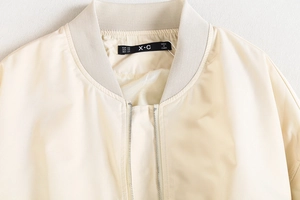 Détail du col côtelé et de la fermeture éclair argentée sur le blouson bomber crème