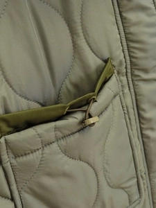 Detail of wavy quilted jacket featuring an adjustable drawstring pocket with green trim