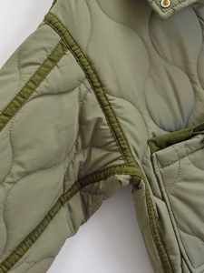Macro detail of wave quilted stitching and side pocket on olive green nylon jacket