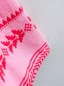 Detailed close-up of pink knit fabric with red ethnic geometric embroidery patterns