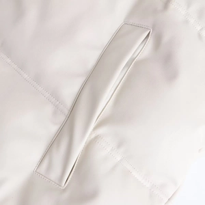 Détail de la texture similicuir crème et coutures doubles précises sur la poche du vêtement