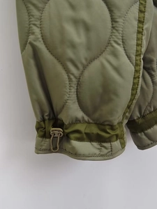 Detail of olive green onion-quilted jacket featuring adjustable drawstring and toggles