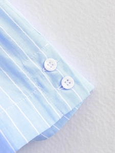 Detail of light blue striped shirt cuff with two white round buttons on twill fabric