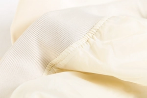 Gros plan du poignet en maille côtelée et du tissu beige lisse de ce blouson bomber