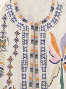 Detailed close-up of colorful floral embroidery on a white bohemian sleeveless vest