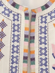 Detailed macro view of colorful geometric embroidery on a white Y2K style sleeveless vest