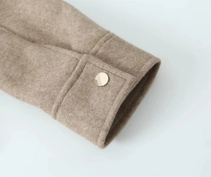Macro detail of soft tweed sleeve with decorative strap and golden metallic button