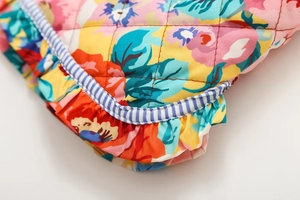 Détail macro du tissu floral matelassé avec imprimés vifs et bordure volantée à rayures bleues