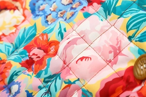 Détail du tissu fleuri matelassé avec surpiqûres en losanges et bouton marron de la veste