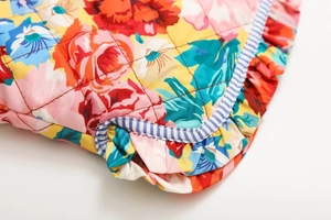 Détail du tissu floral avec matelassage en losanges, bords à volants et liseré rayé