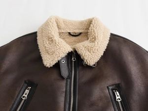 Detail view of dark brown leather jacket with white faux fur collar and silver zipper