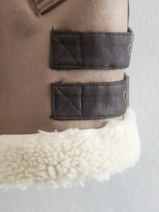 Detailed view of the brown faux suede jacket with metal eyelet straps and white shearling trim