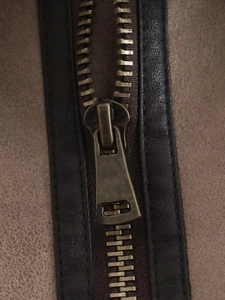 Detailed macro view of vintage bronze metal zipper on a premium brown suede vest jacket