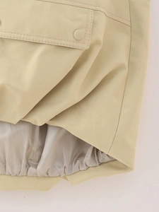 Detail of a beige vest with snap pocket, elastic ruffled hem and smooth fabric texture